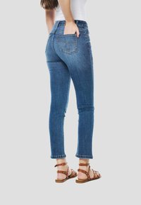 Strakke blauwe spijkerbroek met een taille op middenhoogte, verweerde details en zakstiksels. Gecombineerd met bruine sandalen met studs.