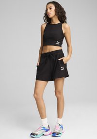Zwart cropped shirt met ribbelstructuur en Puma-logo; gecombineerd met zwarte shorts met trekkoord en levendige, veelkleurige sneakers.