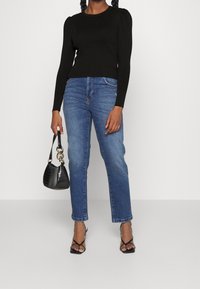 Top noir à manches longues côtelé, jean denim bleu taille haute, sac à main noir à texture crocodile et sandales noires à brides.