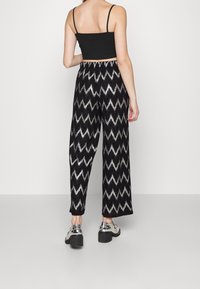 Czarno-srebrne spodnie w zygzakowy wzór o luźnym kroju, z elastycznym pasem i błyszczących metalicznych butach, widziane z tyłu.