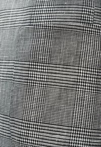 Μοτίβο υφάσματος σε μαύρο και λευκό με ψαροκόκκαλο και καρό, με λεπτομερή υφασμένη υφή και ορατό περίγραμμα τσέπης.