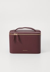 Burgundy cosmetic case with a textured finish, zip closure, and top handle; features gold hardware and subtle branding on the front.