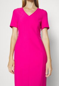Fuchsia jurk met een V-hals, korte mouwen en een aansluitend silhouet. Gemaakt van gladde stof, met strakke lijnen en subtiele naden.