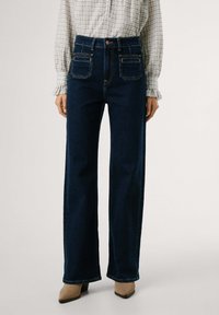 Magas derekú, sötétkék, széles lábú farmernadrág elülső zsebekkel és gombos záródással. Simább denim textúra, látható varrással.