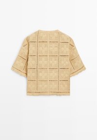 Beżowy krótki sweter dziergany na szydełku z kwiatowymi wzorami w kwadrat i falistymi krawędziami, widoczny od tyłu.