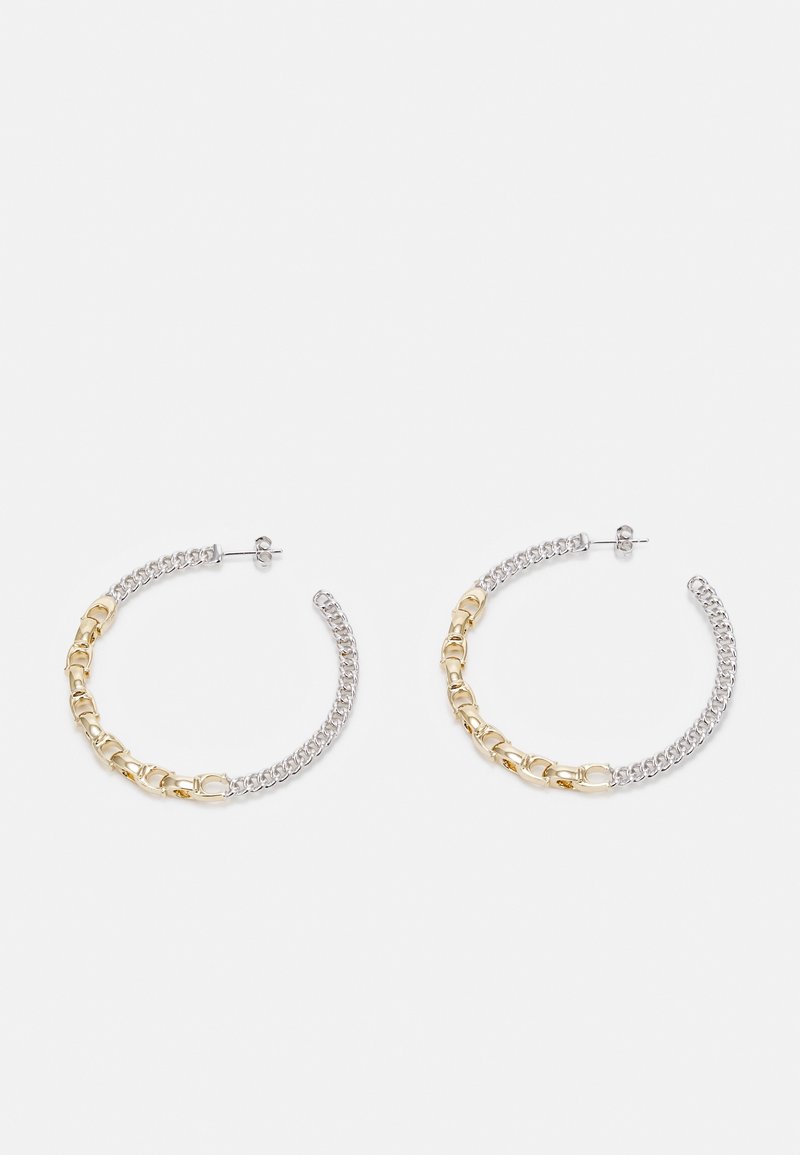 Boucles d'oreilles créoles avec un design moitié chaîne en argent, moitié chaîne en or, fermées par un système à tige et papillon sur fond blanc.