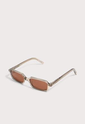 Lunettes de soleil rectangulaires avec montures beige transparent et verres teintés marron posées sur une surface claire.