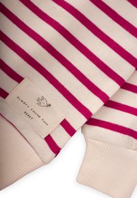 Maglione a righe con colori audaci fucsia e crema. Presenta polsini a coste e un'etichetta tessuta con un grafico di un uccello e testo.