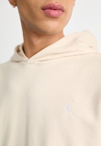 Felpa con cappuccio beige in tessuto morbido con coulisse, caratterizzata da un logo Jumpman bianco ricamato sulla zona sinistra del petto.