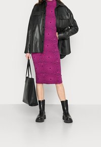 Veste en cuir noir sur une robe à motifs tourbillonnants roses, associée à des bottines noires et à un sac tote noir. Texture lisse et design structuré.