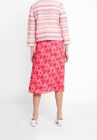 Różowa plisowana spódnica w kwiatowy wzór, zestawiona z teksturowaną czerwoną i białą kurtką w paski oraz białymi mulesami na obcasie.