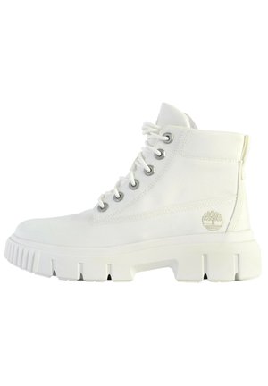 Biały tenisówka za kostkę z grubą, bieżnikowaną podeszwą, metalowymi przelotkami, białymi sznurowadłami i logo Timberland na boku.