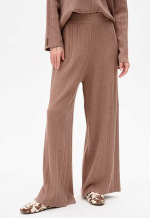 Braune, gerippte weite Hosen mit hohem Bund. Hergestellt aus einem weichen, strukturierten Stoff. Kombiniert mit gemusterten Slippern.