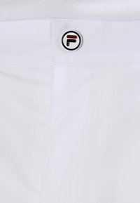 Pantaloni bianchi con un bottone logo circolare nero e rosso in vita, con una texture liscia e dettagli di cucitura puliti.
