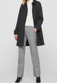 Abrigo de lana gris con cuello de solapa, combinado con pantalones de cuadros grises. Textura suave y corte a medida, acentuado por botines negros.