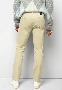 Helle beiger Cordhosen im geraden Schnitt, ausgestattet mit zwei Gesäßtaschen und subtiler Textur, kombiniert mit weißen Sneakers und einem grauen Pullover.
