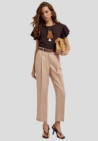 Brown ruffled sleeve top, cream high-waisted trousers, black and brown accent belt, styled with a textured straw bag and strappy heels.