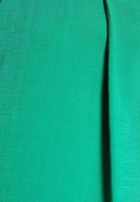 Tessuto verde brillante con una superficie liscia e leggermente textured, caratterizzato da un motivo a reticolo. Il tessuto è piegato da un lato, evidenziando la sua flessibilità.