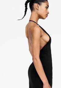 Robe noire sans manches avec un décolleté en V profond et des côtés découpés, présentant une silhouette ajustée et un design minimaliste.