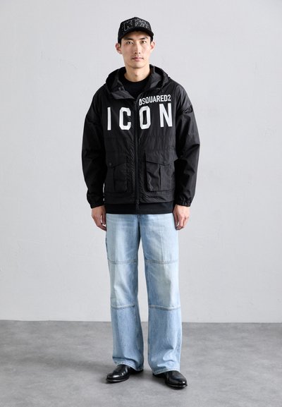 Svart lett hettejakke med stort hvitt trykk "ICON", kombinert med lyseblå brede denimjeans og svarte sko.