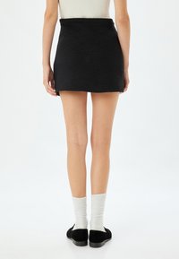 Zwarte mini rok met een rechte zoom, gecombineerd met witte kniesokken en zwarte schoenen, gezien vanaf de achterkant.