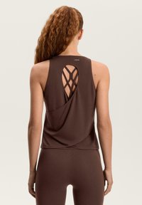 Rjava športna majica brez rokavov z drapirano zadnjo stranjo in prečkano podrobnostjo. Iz gladkega blaga, z diskretno logotipom ob izrezu vratu.