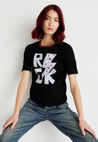 Juodas trumpomis rankovėmis marškinėliai su ryškiu baltu "RISK" grafiku, kuriame pavaizduotas žaibas ir žvaigždės. Kontrastinė bordo spalvos apykaklės detalė.