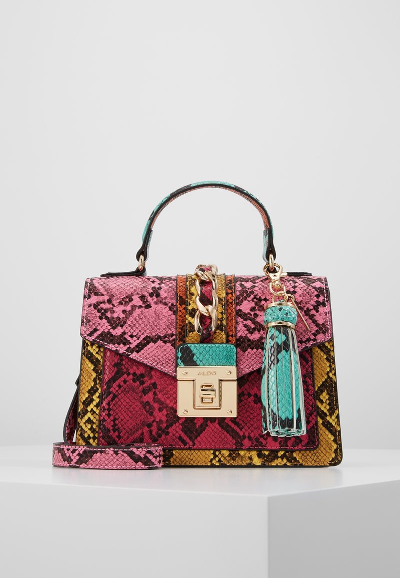 Petit sac à main structuré avec motif multicolore en peau de serpent, chaîne et fermoir dorés, pompon bleu sarcelle, et bandoulière rose sur une surface blanche.