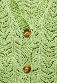 Cardigan tricoté vert clair avec un motif de feuilles, orné d'un bouton marron à deux trous à l'avant. Texture douce avec des détails de couture complexes.