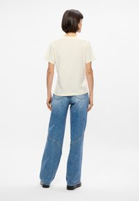 Κρέμ T-shirt με κοντά μανίκια, συνδυασμένο με ανοιχτό γαλάζιο τζιν σε ευρεία γραμμή με καμπύλες ραφές και κλασική εφαρμογή.