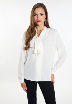 Bluză albă cu un nod în față, cu nasturi pe față, mâneci lungi și țesătură netedă, asortată cu pantaloni negri. Prezintă un design clasic.