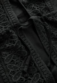 Čierna tkanina s kvetinovými krajkami a detailom na viazanie popruhu pozdĺž švu alebo otvoru.