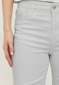 Světle šedé džíny s přiléhavým střihem, které mají přední kapsy, malý stříbrný knoflík a prošití podél švů.