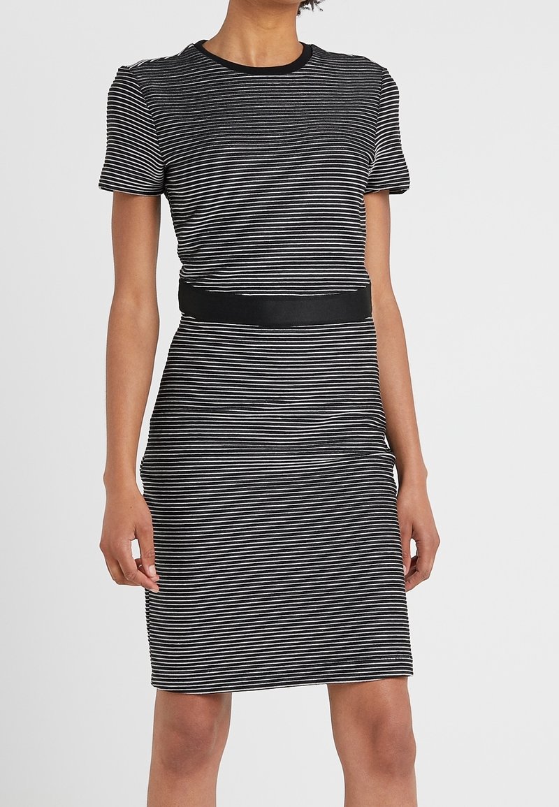 Robe à rayures noires et blanches avec manches courtes, encolure ronde, et une ceinture noire soulignant la taille. Confectionnée en tissu lisse et extensible.