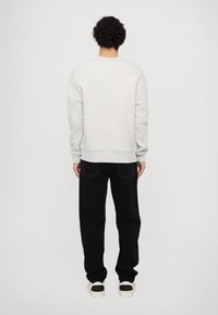 Felpa grigia con scollo rotondo, maniche lunghe e polsini a coste, abbinata a pantaloni neri e sneakers bianche. Design semplice, dettagli minimi.