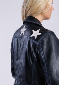 Czarna skórzana kurtka o gładkiej fakturze, ozdobiona srebrnymi aplikacjami w kształcie gwiazd na ramionach, prezentująca klasyczny design.
