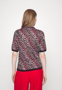 Stricktop mit floralem Muster in Pink und Lila auf schwarzem Hintergrund, mit kurzen Ärmeln und schwarzen Rippakzenten.