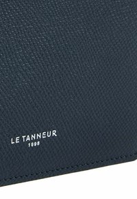 Portafoglio in pelle testurizzata blu con motivo embossato, caratterizzato dal nome della marca "LE TANNEUR 1898" in lettere bianche. Design pulito e bordi definiti.