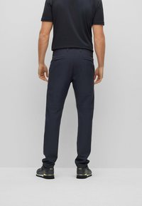 Navy trousers with a slim fit, featuring two back pockets and a smooth texture. Paired with dark footwear and a black shirt.