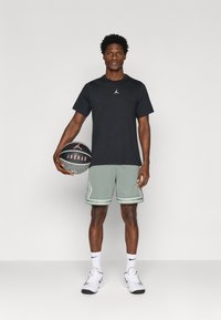 Svart kortermet skjorte med Jordan-logo, lysegrønne mesh-shortser med hvite detaljer, svart og grå basketball, hvite joggesko.