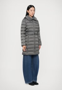 Γκρι επενδυμένο παλτό με γούνινο γιακά, στενή μέση και δύο εμπρόσθιες τσέπες. Συνδυασμένο με φαρδιά τζιν παντελόνια και μαύρα παπούτσια.