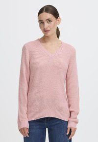 Maglione lavorato a maglia rosa con scollo a V, maniche lunghe e polsini a coste. Il materiale ha una finitura texturizzata e una vestibilità leggermente ampia.