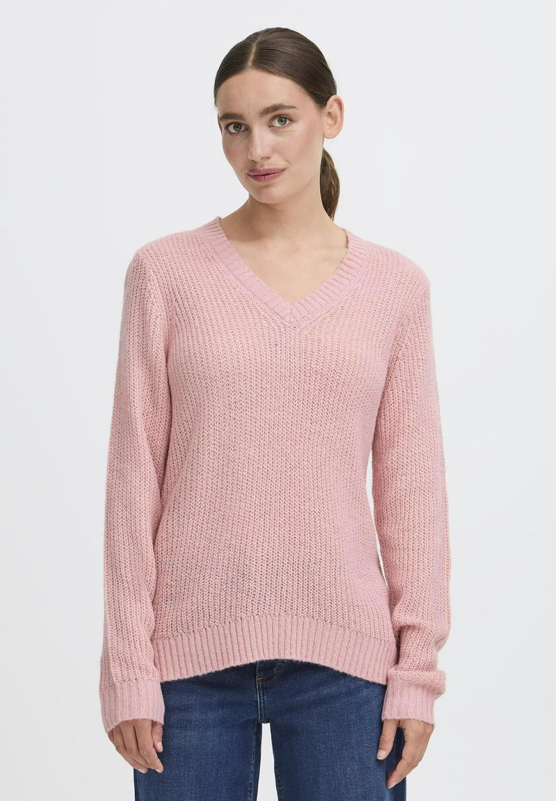 Maglione lavorato a maglia rosa con scollo a V, maniche lunghe e polsini a coste. Il materiale ha una finitura texturizzata e una vestibilità leggermente ampia.
