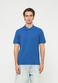 Μπλε πόλο πουκάμισο από απαλό βαμβάκι, με κλασικό γιακά, κοντά μανίκια και 3 κουμπιά στην πατιλέτα. Διακριτικό λογότυπο στο στήθος.