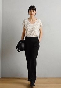 Haut beige clair à motif léopard avec des manches courtes, associé à un pantalon noir et un sac noir texturé, présentant une texture lisse et plate.