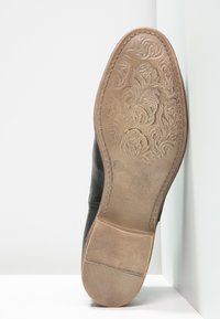 Scarpa in pelle nera con una parte superiore testurizzata, caratterizzata da una suola in gomma goffrata dettagliata e un tacco liscio, vista dal basso.