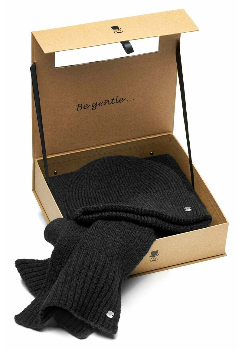 Black ribbed knit beanie and scarf set inside an open cardboard gift box with "Be gentle..." printed on the lid interior.