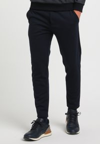 Marineblå joggerbukser med en tilspidset design, elastisk talje og sidelommer, parret med mørke sneakers med en lys såleaksecent.