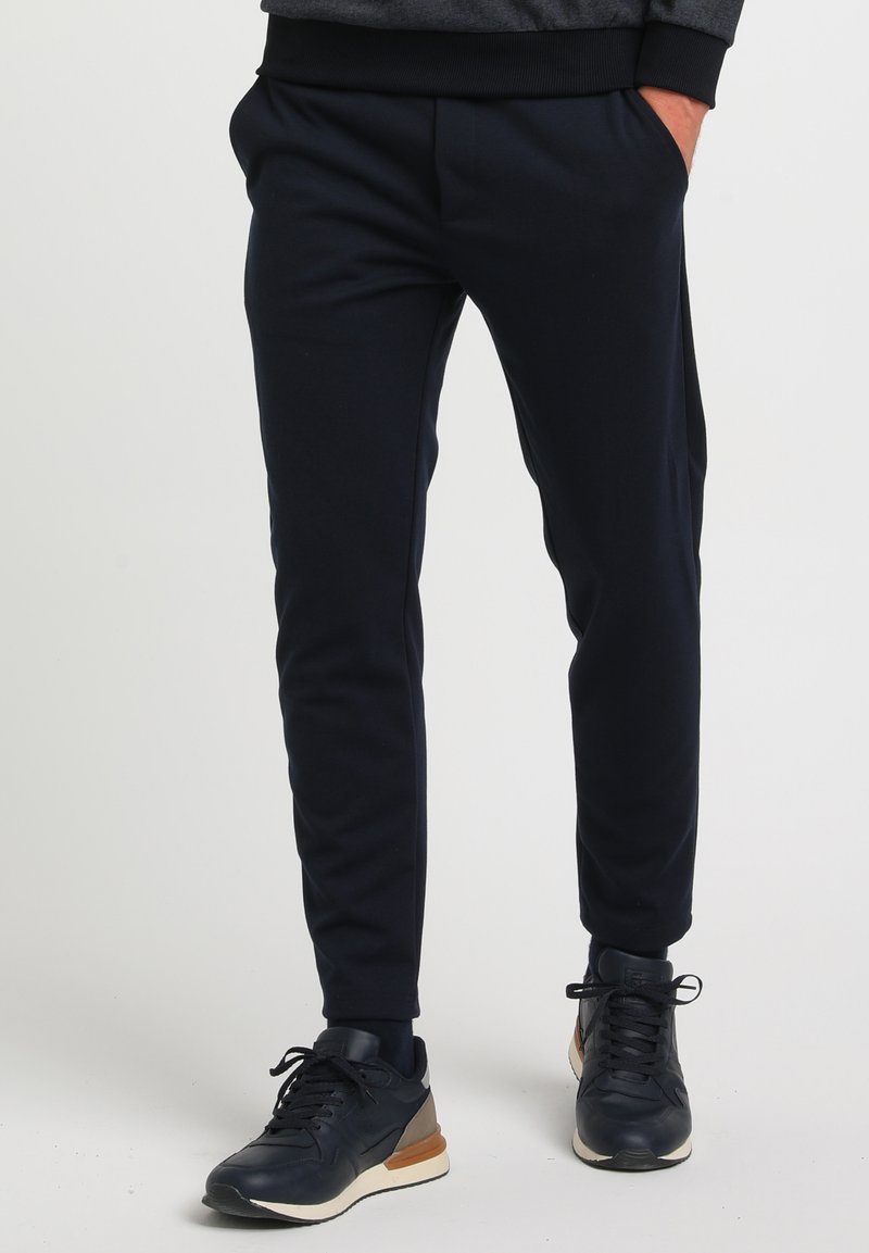 Marineblå joggerbukser med en tilspidset design, elastisk talje og sidelommer, parret med mørke sneakers med en lys såleaksecent.