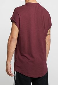 Camiseta de manga corta de color burdeos con cuello redondo, material de algodón suave, corte holgado, dobladillo curvado y detalle sutil de etiqueta lateral.